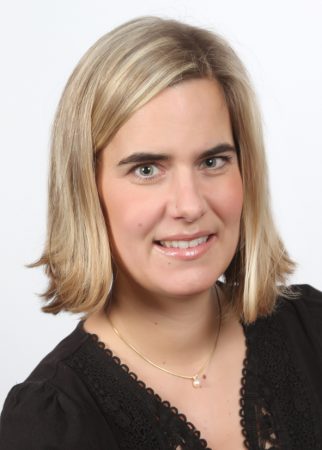 Frau mit schulterlangen blonden Haaren, schwarzem Oberteil und Halskette vor hellem Hintergrund.