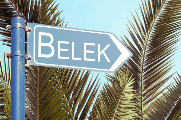 Straßenschild mit der Aufschrift ‚Belek‘ vor Palmen im Hintergrund.