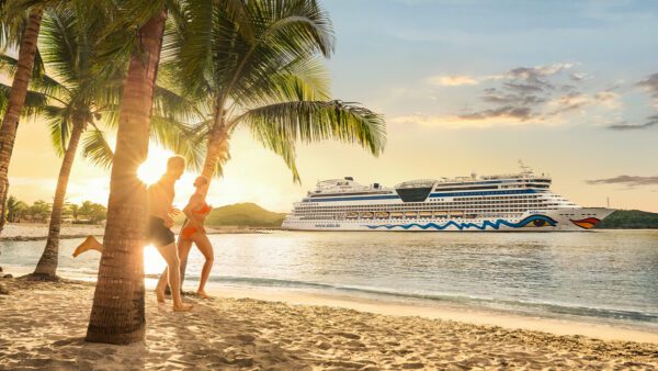 Zwei Personen spielen fröhlich an einem Strand unter Palmen bei Sonnenuntergang, während ein großes Kreuzfahrtschiff im Wasser im Hintergrund vorbeifährt.