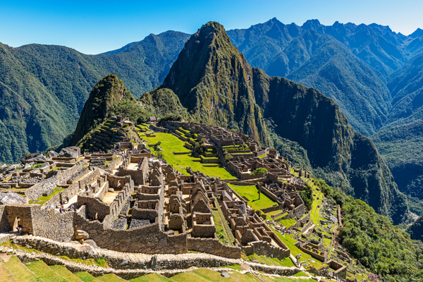 Panoramablick auf die antiken Ruinen von Machu Picchu in Peru, umgeben von grünen Bergen und einer klaren blauen Himmel.