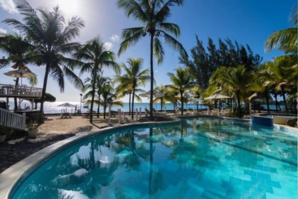Das Bild zeigt eine Poolandschaft mit vielen Palmen im Hintergrund wodurch die Sonne scheint auf Mauritius.